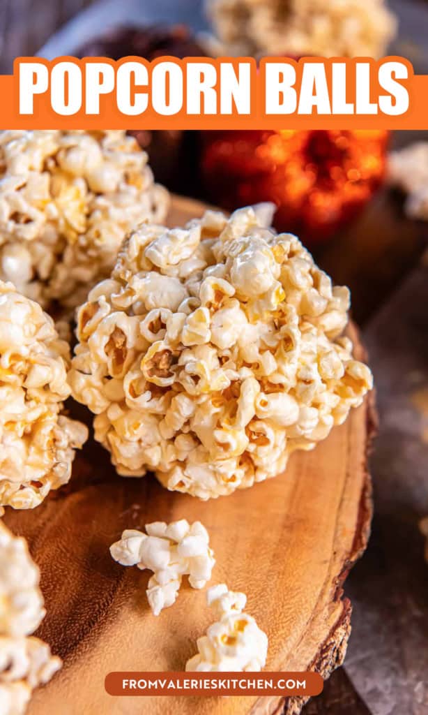 Stack of homemade caramel popcorn balls on a wooden serving board with glittery pumpkins in the background with text overlay.