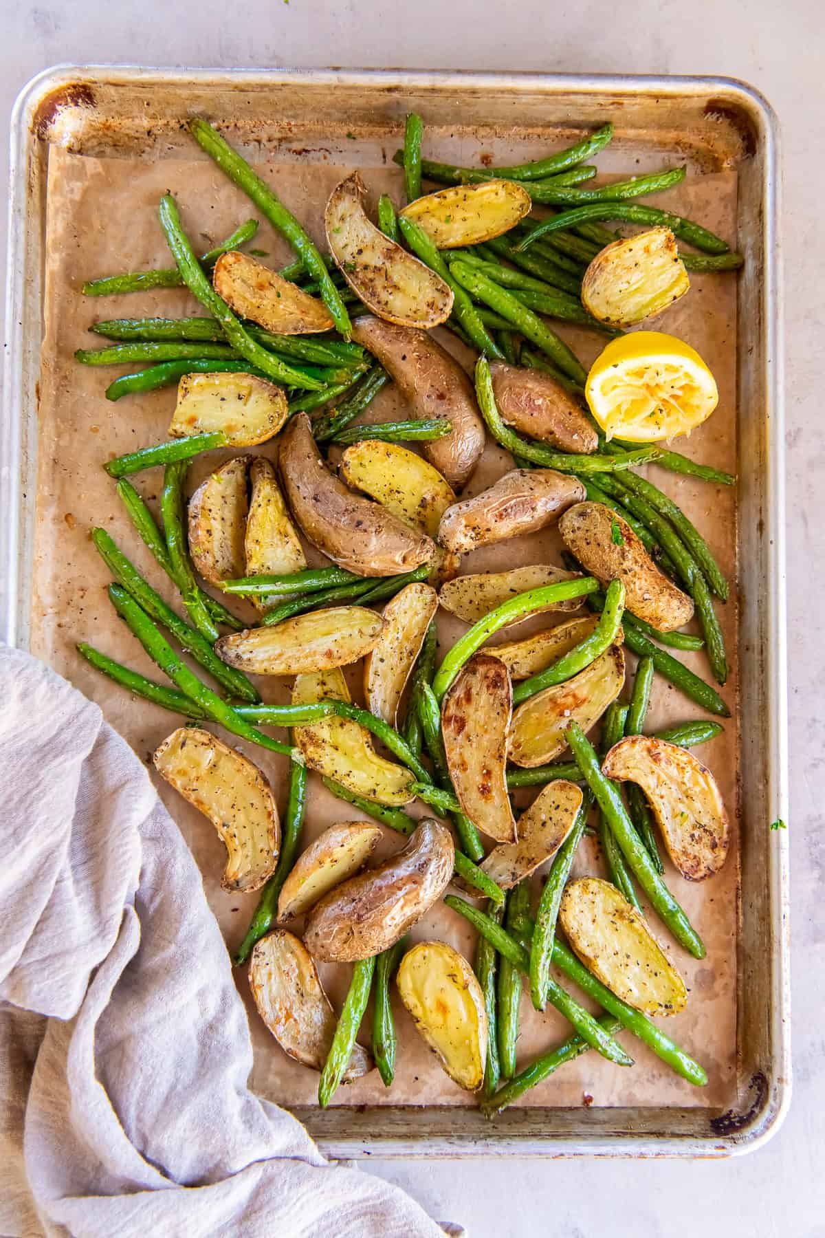 Roasted fingerling potatoes and green beans on a sheet plan with a lemon half.