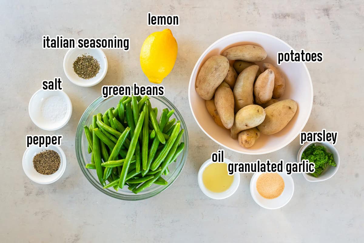 Fingerling potatoes, green beans, a lemon, oil, and spices in bowls with text overlay.