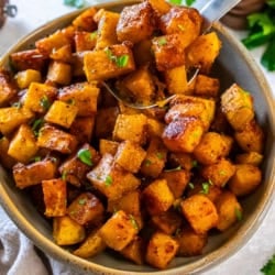 Caramelized roasted butternut squash cubes served in a bowl with a spoon and garnished with parsley.