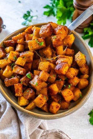 Caramelized roasted butternut squash cubes served in a bowl with a spoon and garnished with parsley.
