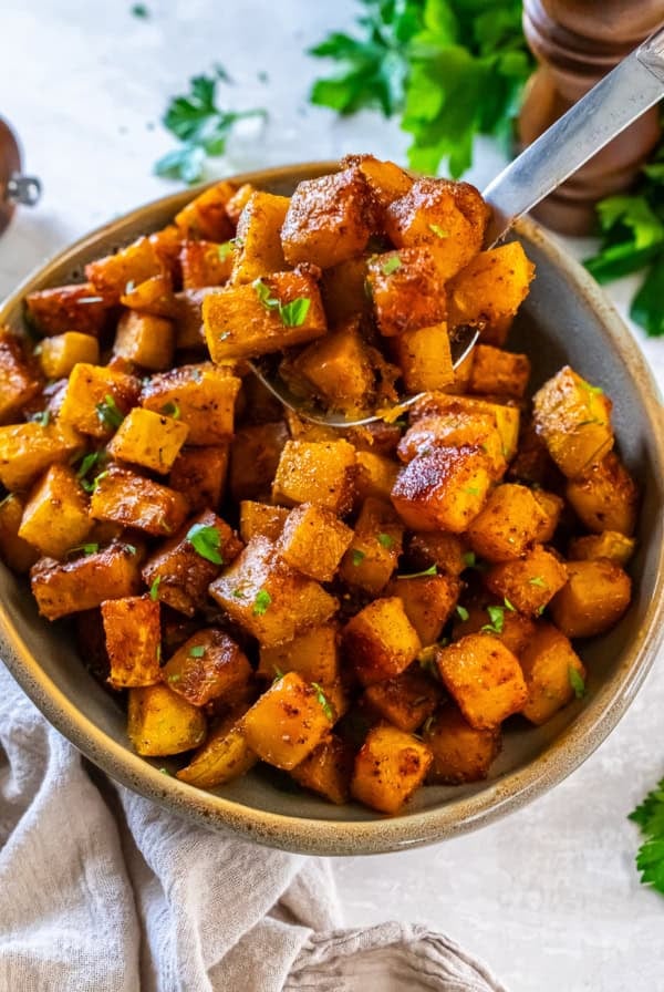 Caramelized roasted butternut squash cubes served in a bowl with a spoon and garnished with parsley.