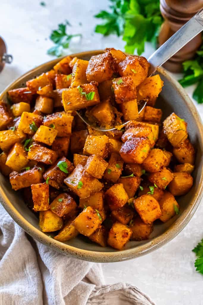 Caramelized roasted butternut squash cubes served in a bowl with a spoon and garnished with parsley.