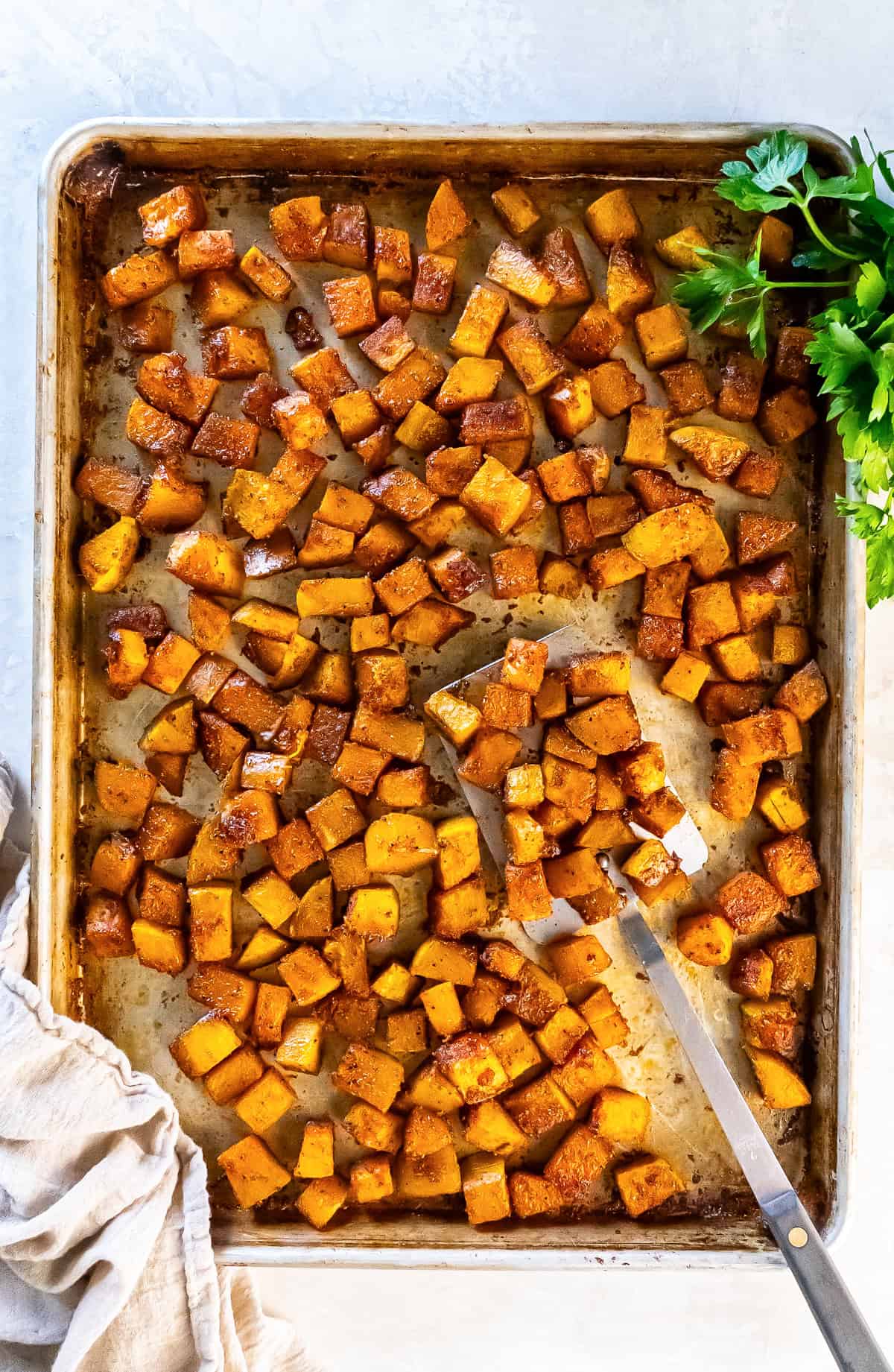 Roasted butternut squash cubes on a sheet pan with a spatula and parsley.