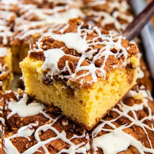 Slice of cake mix coffee cake lifted from the pan, topped with chopped pecans and a drizzle of white icing.