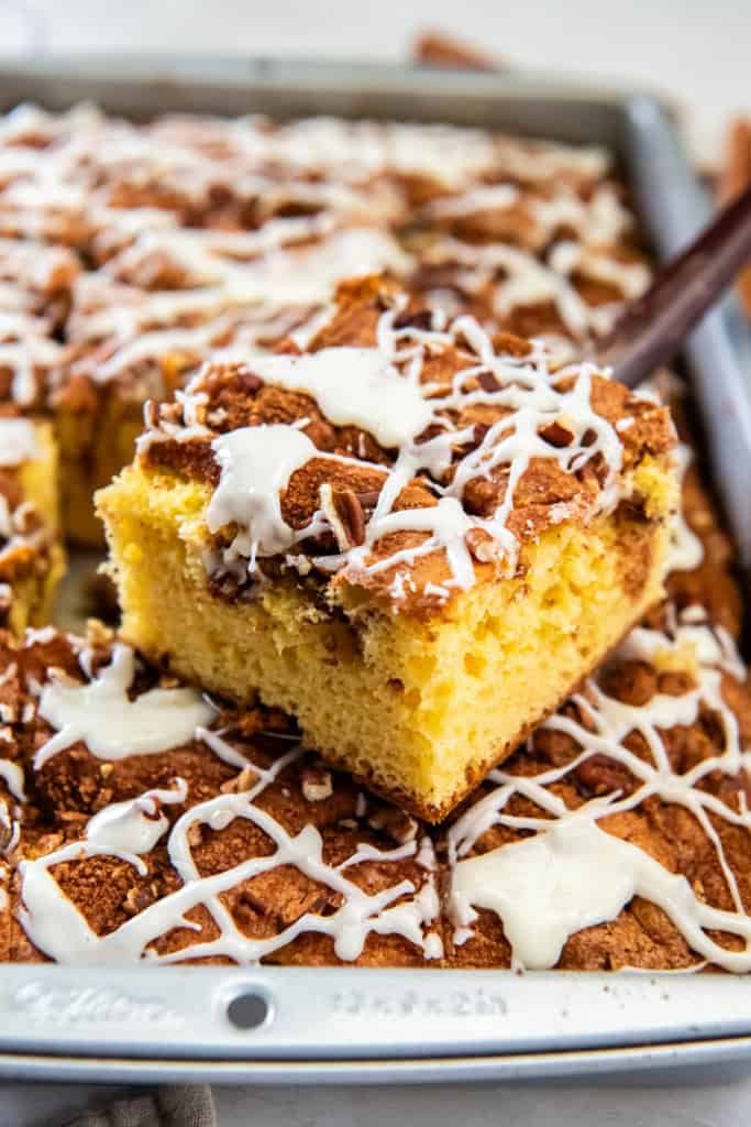 Slice of cake mix coffee cake lifted from the pan, topped with chopped pecans and a drizzle of white icing.