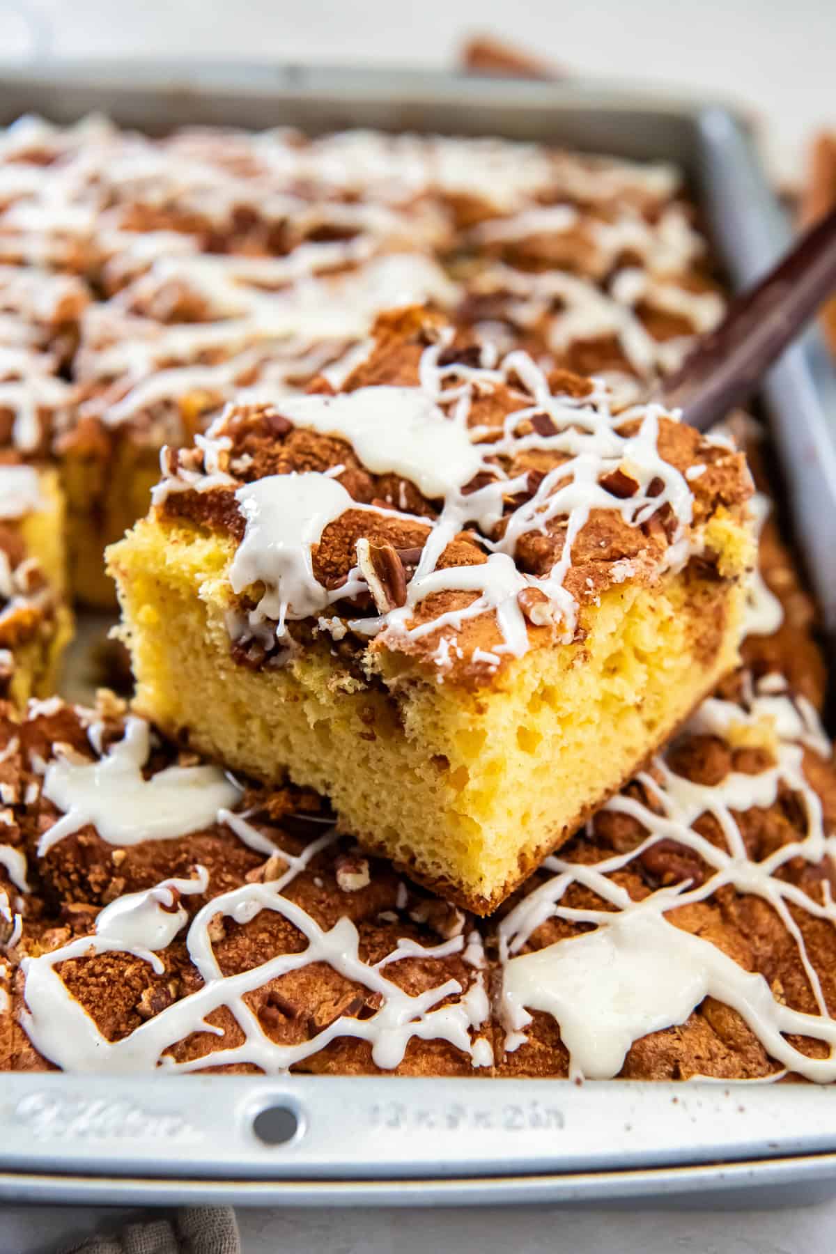 Slice of cake mix coffee cake lifted from the pan, topped with chopped pecans and a drizzle of white icing.
