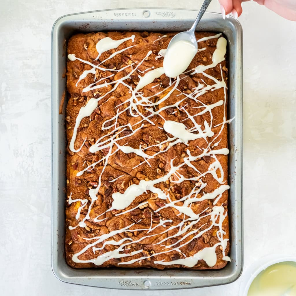 A spoon drizzling icing over a coffee cake in a metal pan.