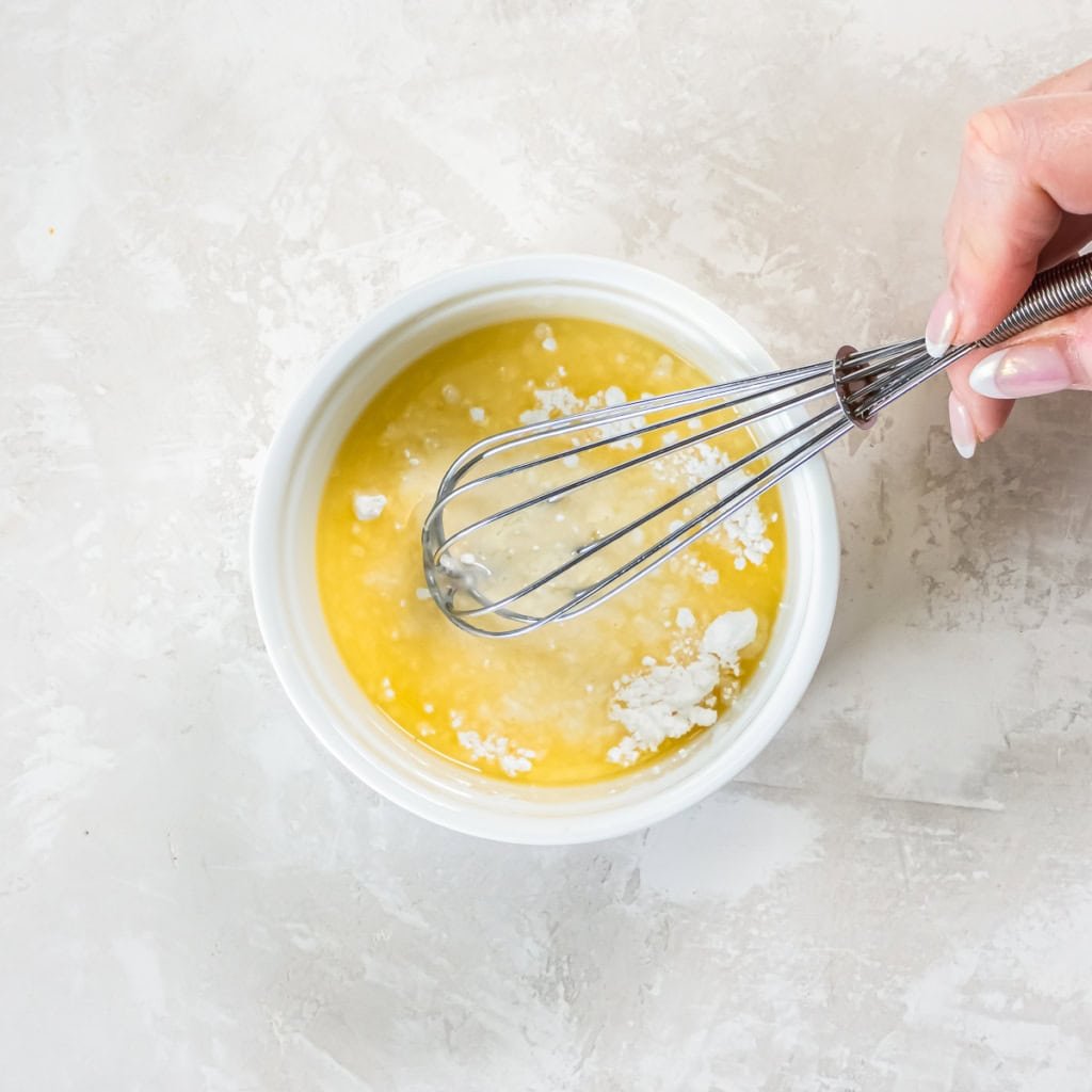 A hand using a small whisk to combine powdered sugar and orange juice.