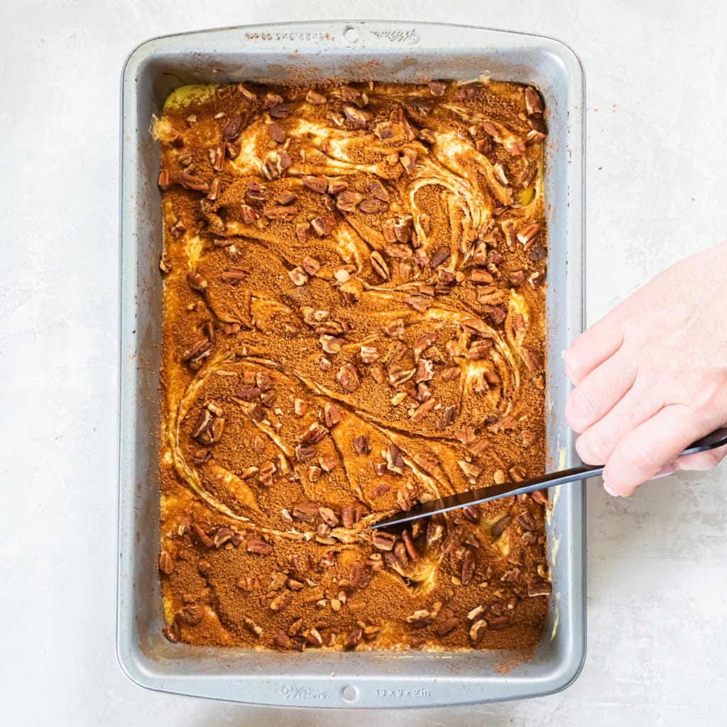 A knife swirling a sugar pecan mixture into cake batter.