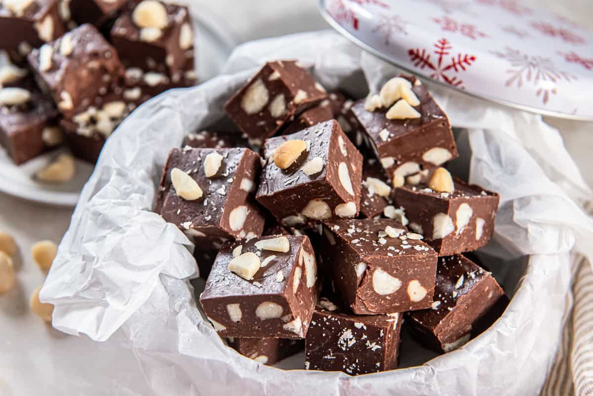 Macadamia nut fudge piled in a gift tin with parchment paper and holiday decor.