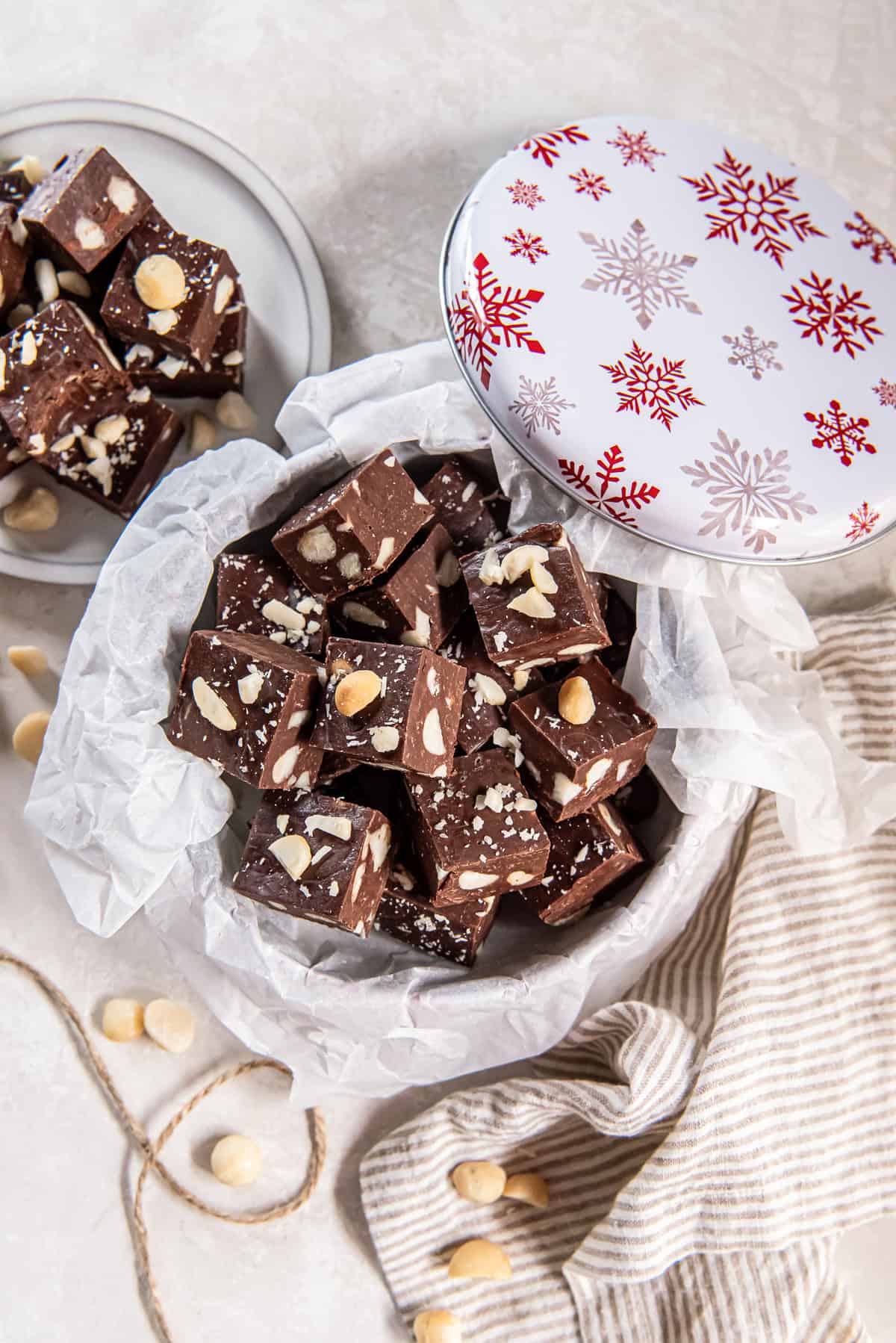 Macadamia nut fudge piled in a gift tin with parchment paper and holiday decor.