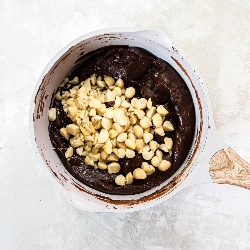 Macadamia nuts on top of a chocolate fudge mixture in a saucepan.