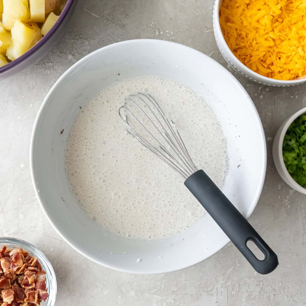A whisk resting in a bowl filled with a sour cream mixture.