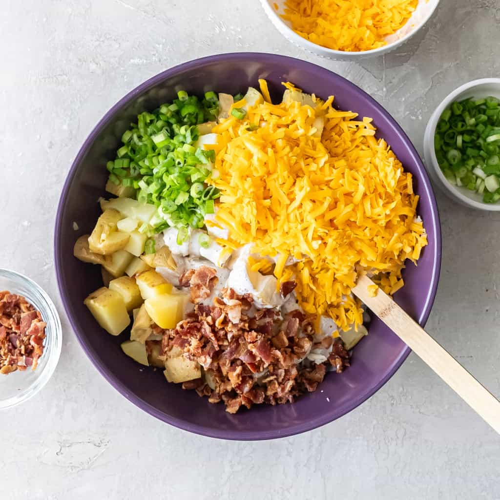 Chopped potatoes topped with shredded cheddar, green onions, and crumbled bacon before mixing.