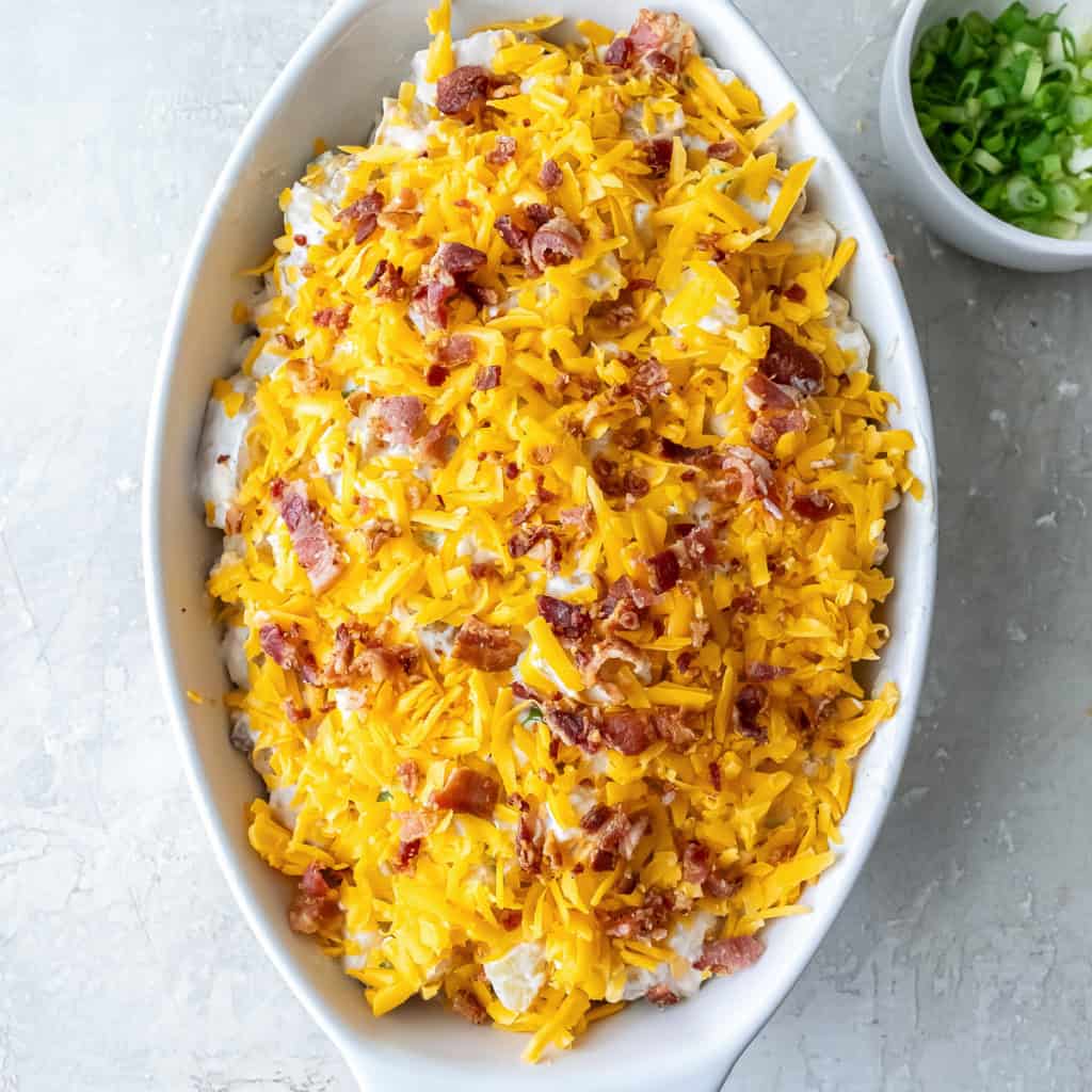 Twice Baked Potato Casserole topped with shredded cheddar and crumbled bacon, ready for the oven.