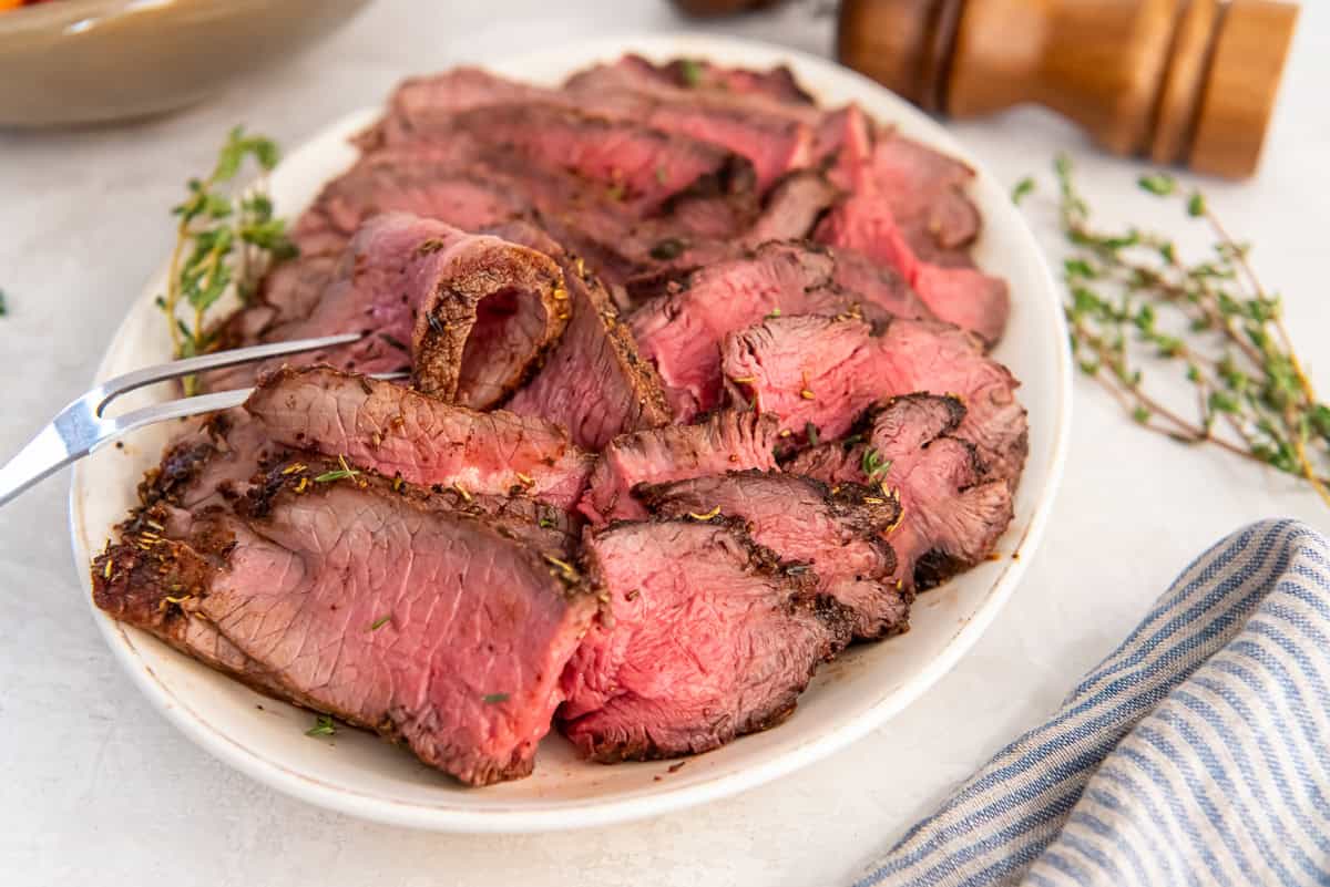 Air fryer sirloin tip roast sliced thin and cooked to medium-rare, arranged on a serving platter.