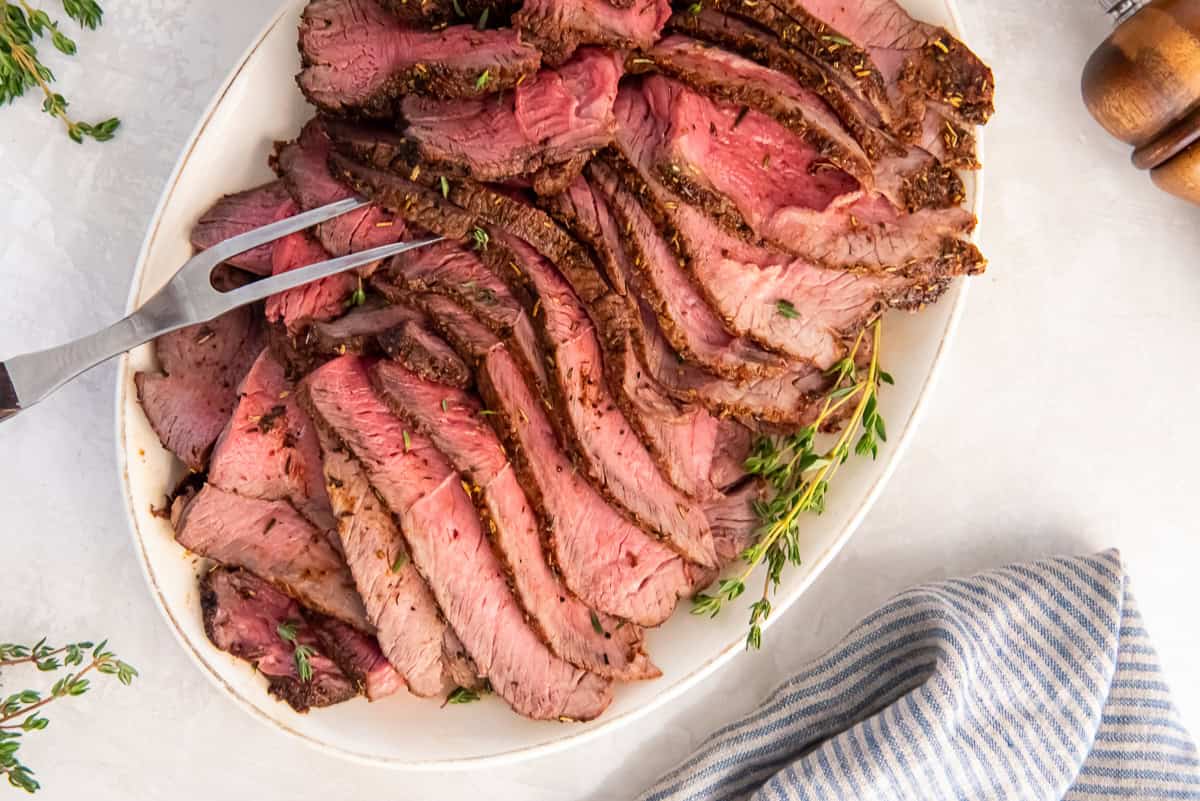 Close-up of sliced air fryer sirloin tip roast with a browned exterior and pink center on a platter.