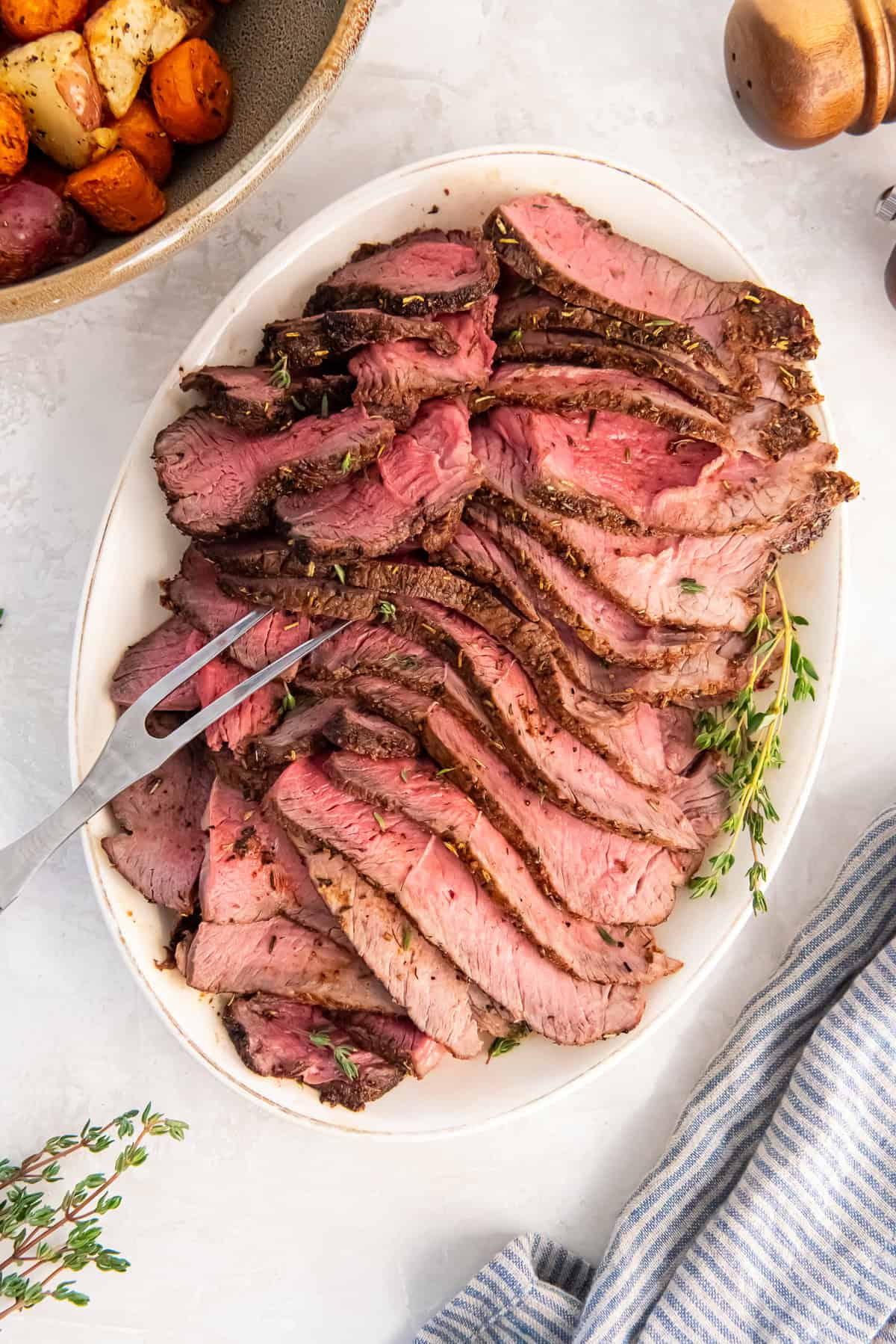 Platter of sliced air fryer sirloin tip roast served medium-rare, with roasted vegetables in the background.