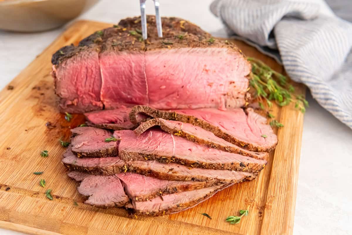 Close-up of sliced air fryer sirloin tip roast with a browned exterior and pink center on a platter.