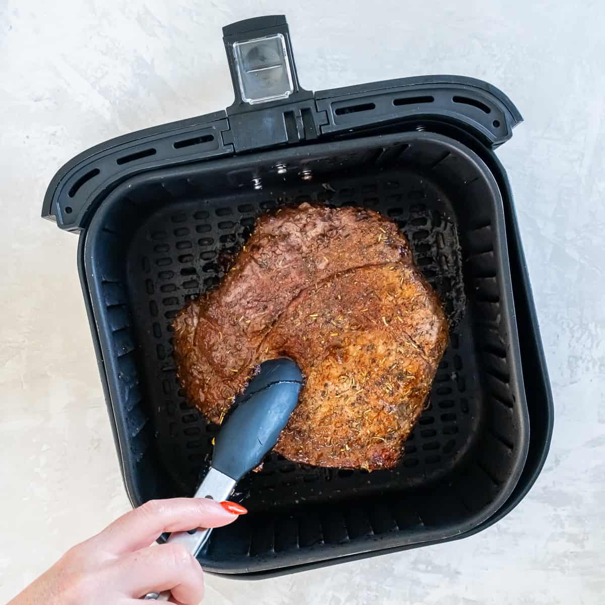 Using tongs to flip a sirloin tip roast in the air fryer basket during cooking.