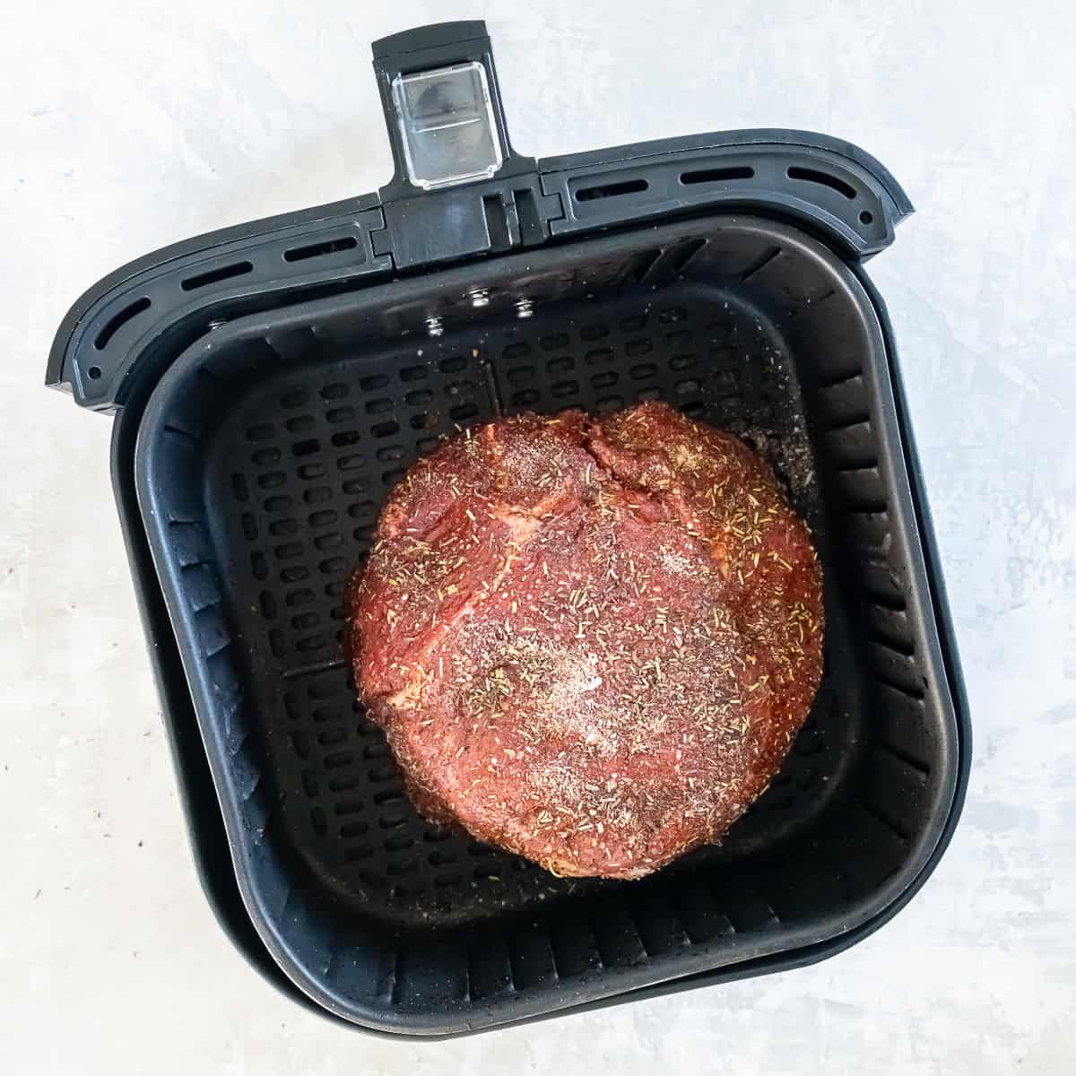 Seasoned sirloin tip roast placed in the air fryer basket before cooking.