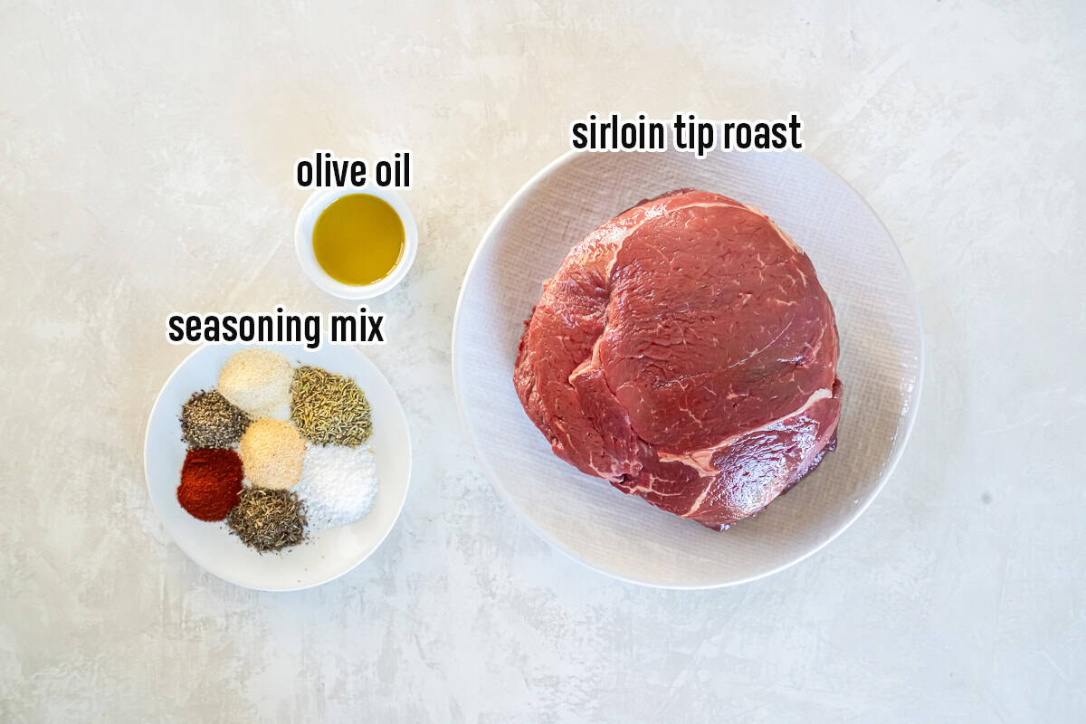 Ingredients for air fryer roast beef including a sirloin tip roast, olive oil, and a homemade roast beef seasoning mix on a light surface.