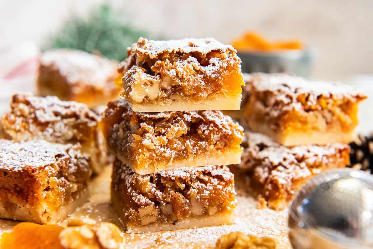 Stacked apricot bars showing the shortbread crust and chunky apricot-walnut filling, dusted with powdered sugar.