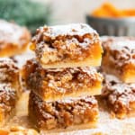 Stacked apricot bars showing the buttery shortbread crust and chewy apricot-walnut filling, dusted with powdered sugar.