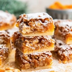 Stacked apricot bars showing the buttery shortbread crust and chewy apricot-walnut filling, dusted with powdered sugar.