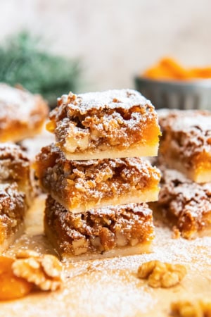 Stacked apricot bars showing the buttery shortbread crust and chewy apricot-walnut filling, dusted with powdered sugar.