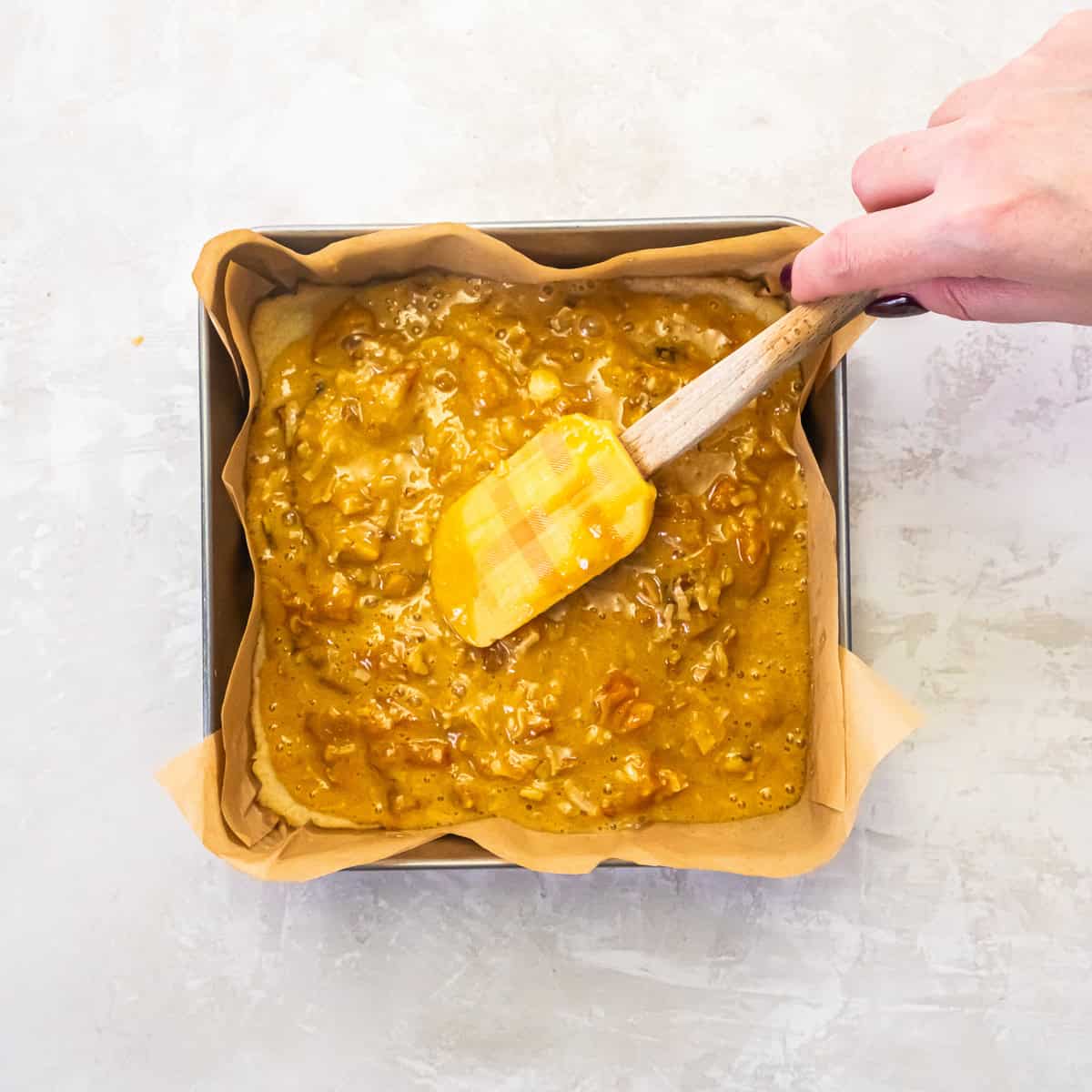 Apricot bar topping being spread evenly over the baked crust in a square pan.