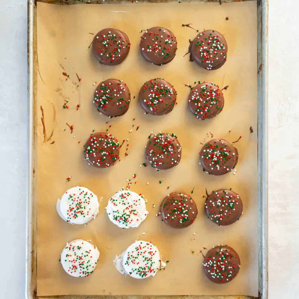 Chocolate- and white-chocolate–dipped peanut butter Ritz cookies arranged on a parchment-lined baking sheet and topped with holiday sprinkles.