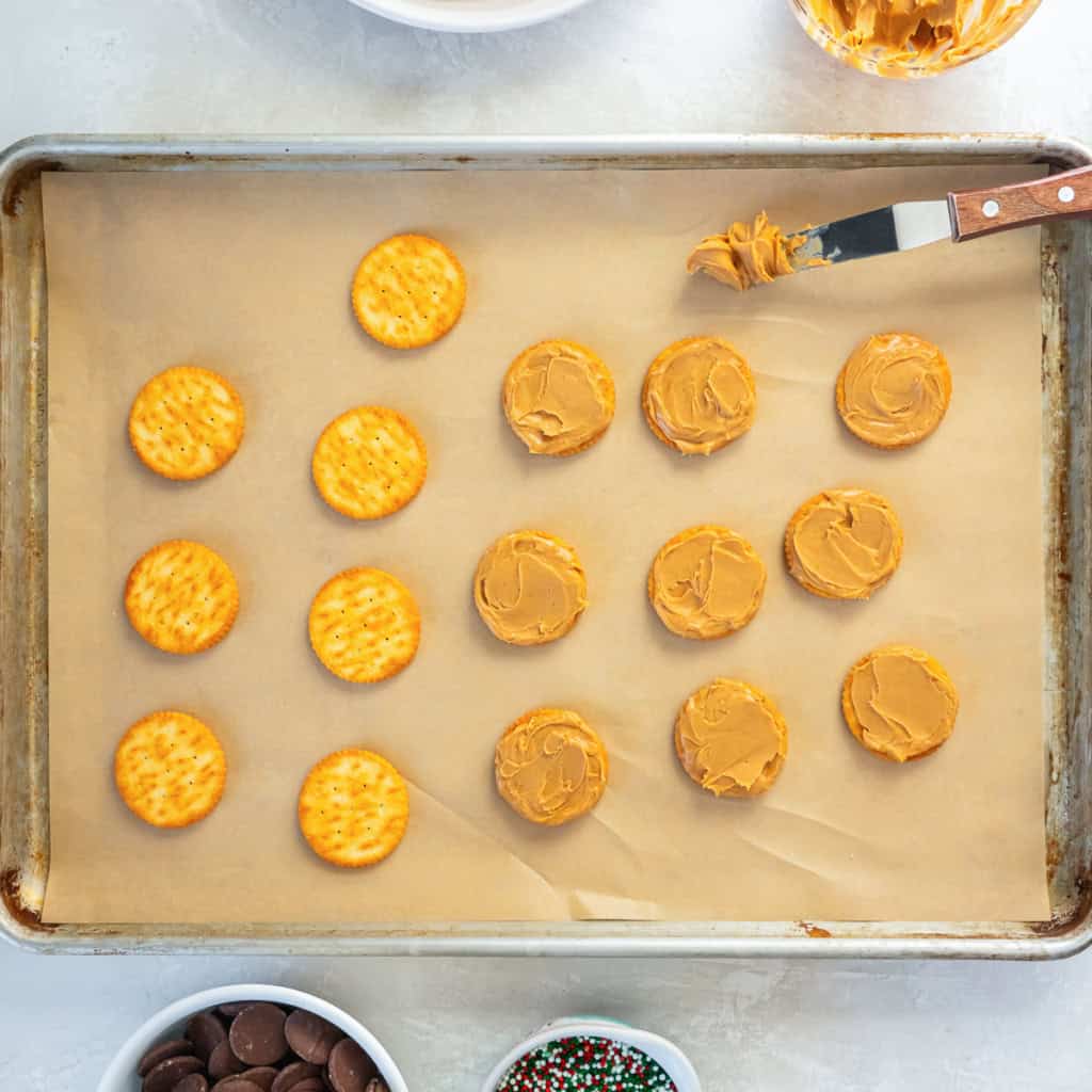 Ritz crackers topped with peanut butter arranged on a parchment-lined baking sheet, ready to be assembled into sandwich cookies.