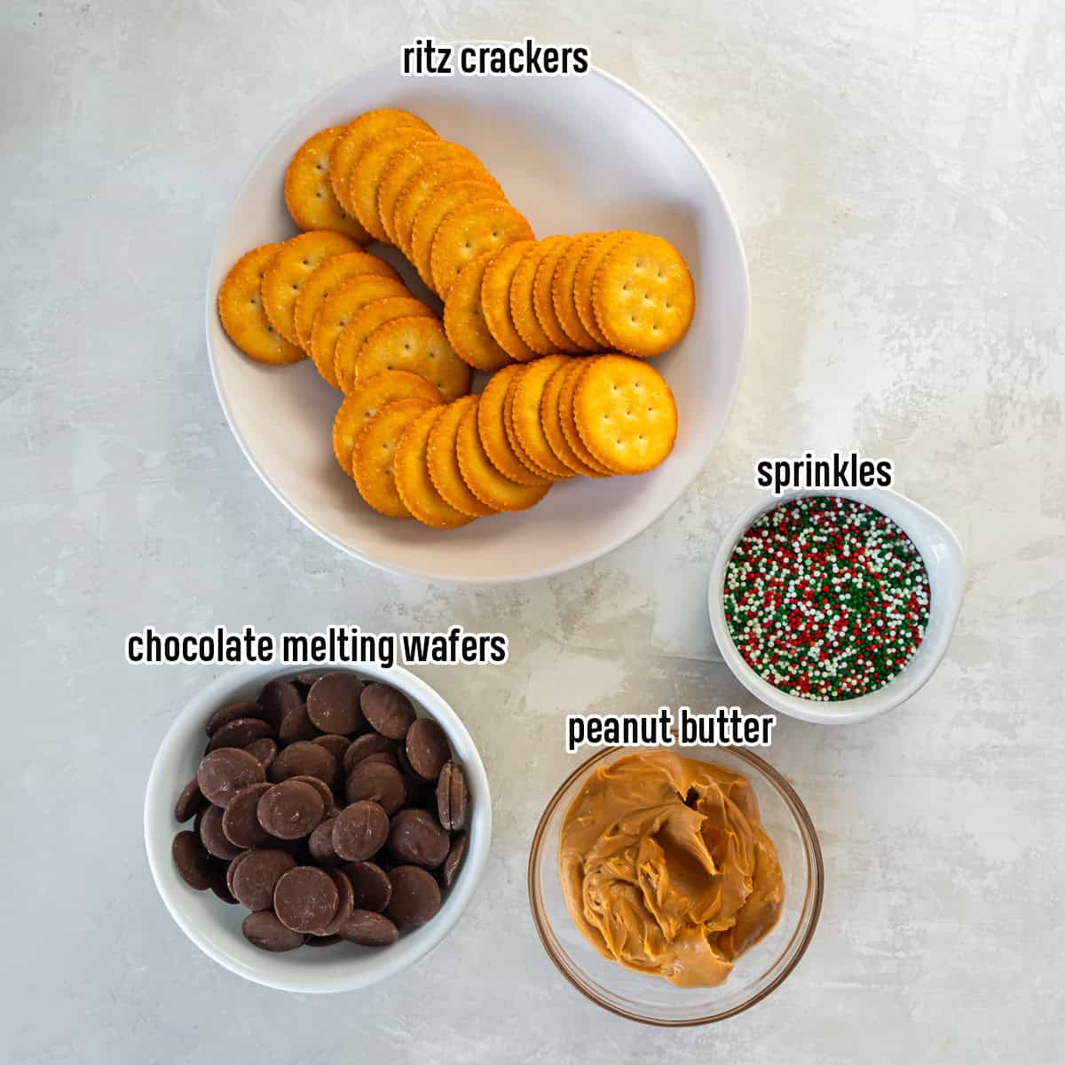 the ingredients for chocolate-dipped peanut butter Ritz cookies, including a bowl of Ritz crackers, chocolate melting wafers, peanut butter, and holiday sprinkles.