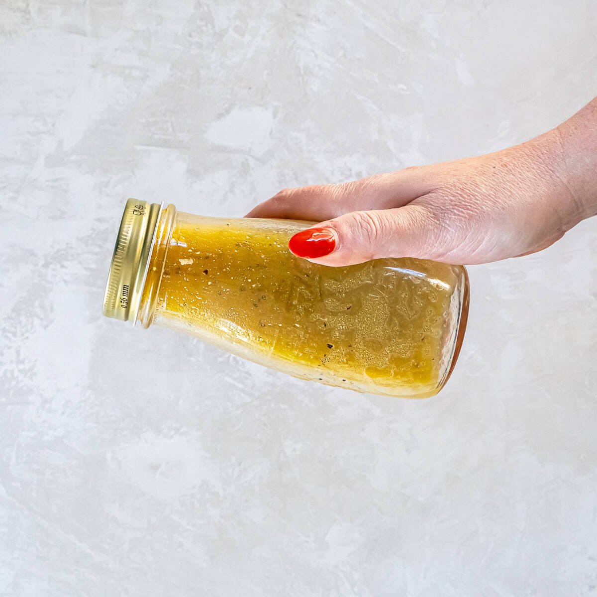 Hand holding a jar of Maple Dijon Vinaigrette and shaking it to combine and emulsify the dressing.