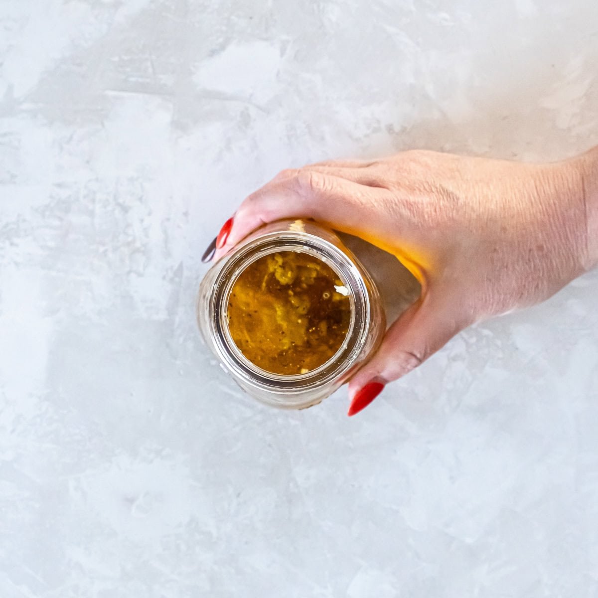Top-down view of a hand holding an open jar of Maple Dijon Vinaigrette showing the ingredients in the jar.