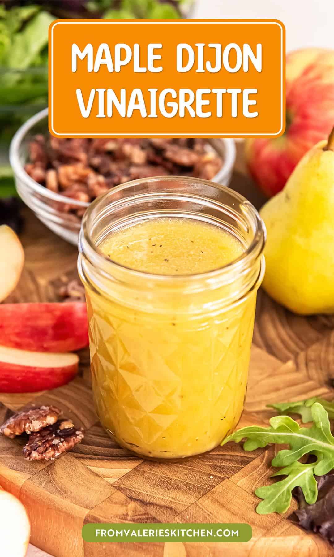 Top-down view of a jar of Maple Dijon Vinaigrette on a wooden board with candied pecans, apples, greens, and pears with text overlay.