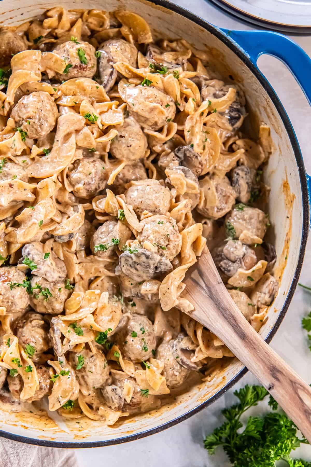 Creamy meatball stroganoff with wide egg noodles and mushrooms in a blue skillet, wooden spoon tucked into the noodles, sprinkled with parsley.