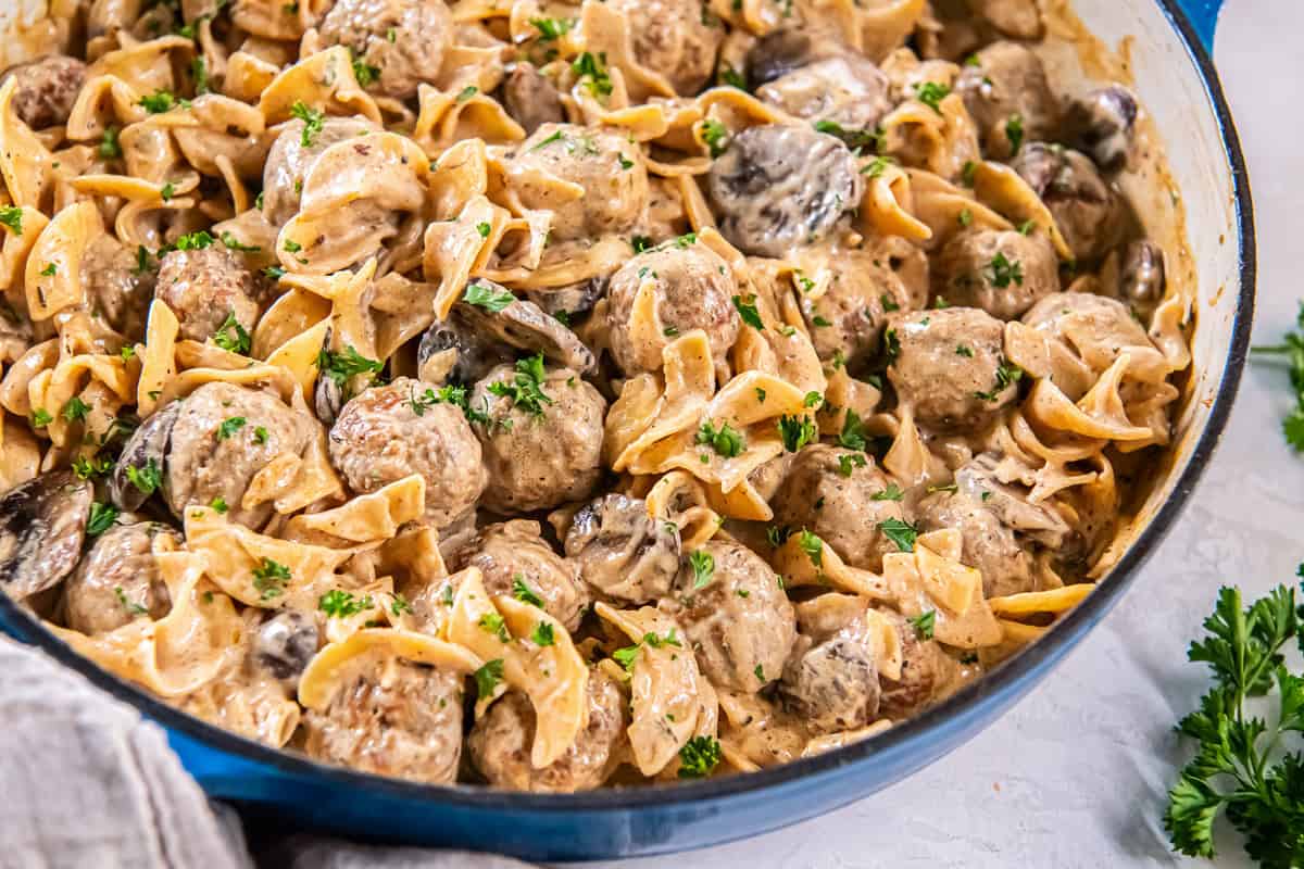 Skillet of creamy meatball stroganoff with wide egg noodles and mushrooms, sprinkled with parsley.