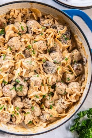 Creamy Meatball Stroganoff with wide egg noodles, mushrooms, and meatballs in a skillet, sprinkled with chopped parsley.