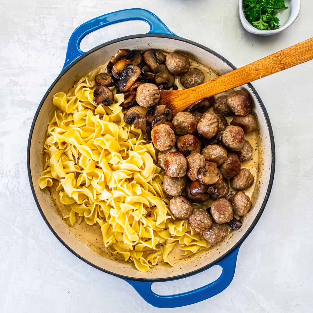 Cooked egg noodles, browned meatballs, and sautéed mushrooms added back to the pan over the creamy sauce, ready to mix.