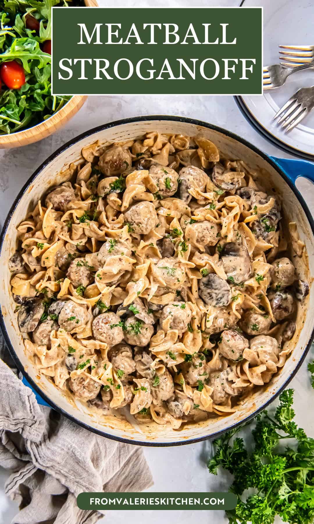 Creamy Meatball Stroganoff with wide egg noodles, mushrooms, and meatballs in a blue-handled skillet, topped with chopped parsley, with a green salad and plates with forks nearby with text overlay.