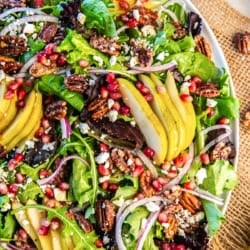 A colorful Pear Pomegranate Salad with sliced pears, mixed baby greens, pomegranate arils, red onion, glazed pecans, and feta arranged on a white serving platter.