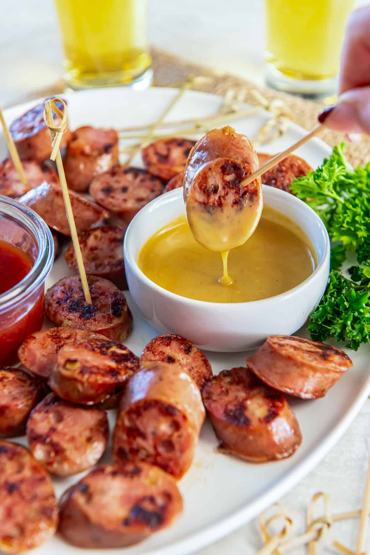 Chicken sausage bite dipped into creamy honey mustard sauce, showing the thick texture of the dip on a white serving platter.