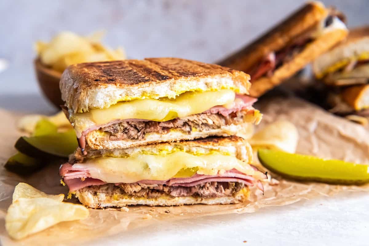 A pressed Cuban sandwich showing layers of roast pork, ham, melted Swiss cheese, pickles, and mustard on golden toasted bread.