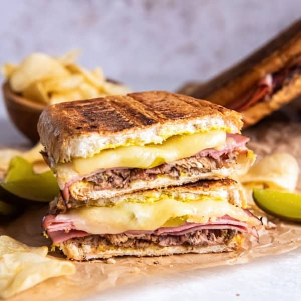 A pressed Cuban sandwich showing layers of roast pork, ham, melted Swiss cheese, pickles, and mustard on golden toasted bread.