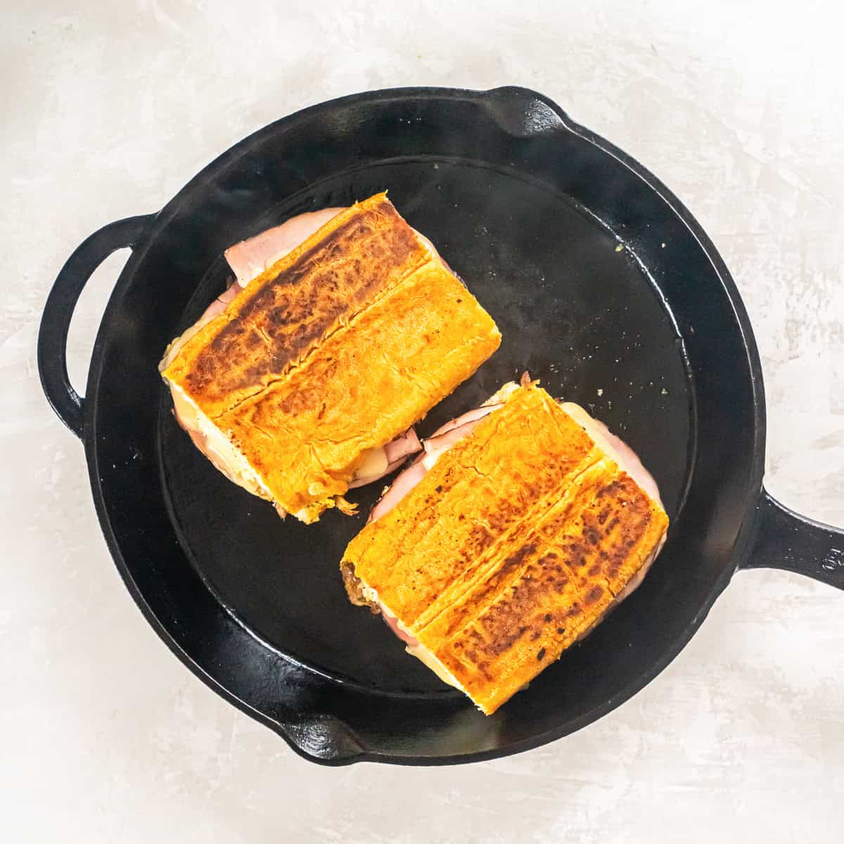 Cuban sandwiches pressed in a cast iron skillet until golden brown and toasted.