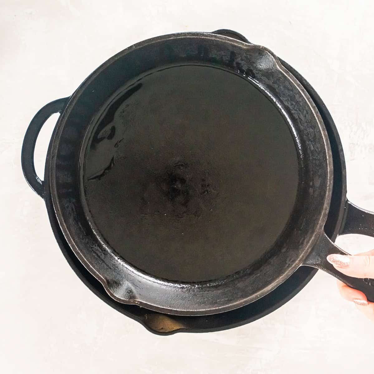 A second cast iron skillet being placed over the sandwiches to press them while cooking.