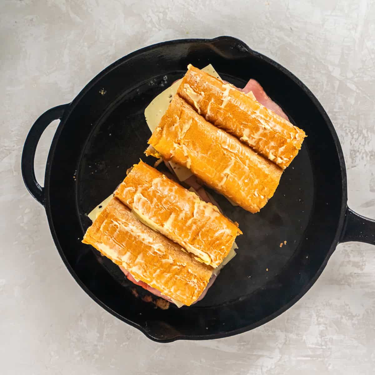 Two Cuban sandwiches in a preheated cast iron skillet.